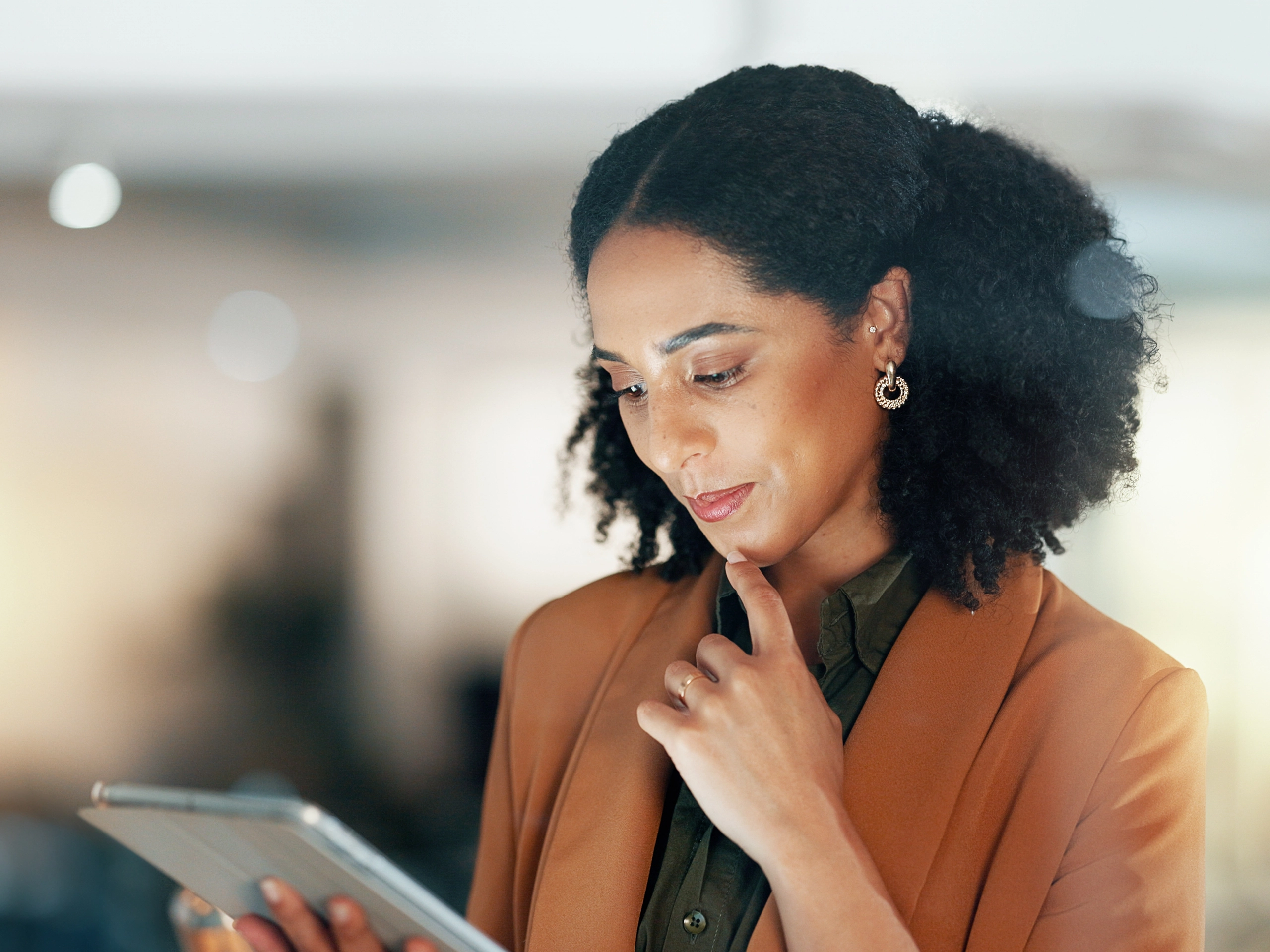 Indoor portrait shows individual reviewing tablet thoughtfully in softly lit professional environment