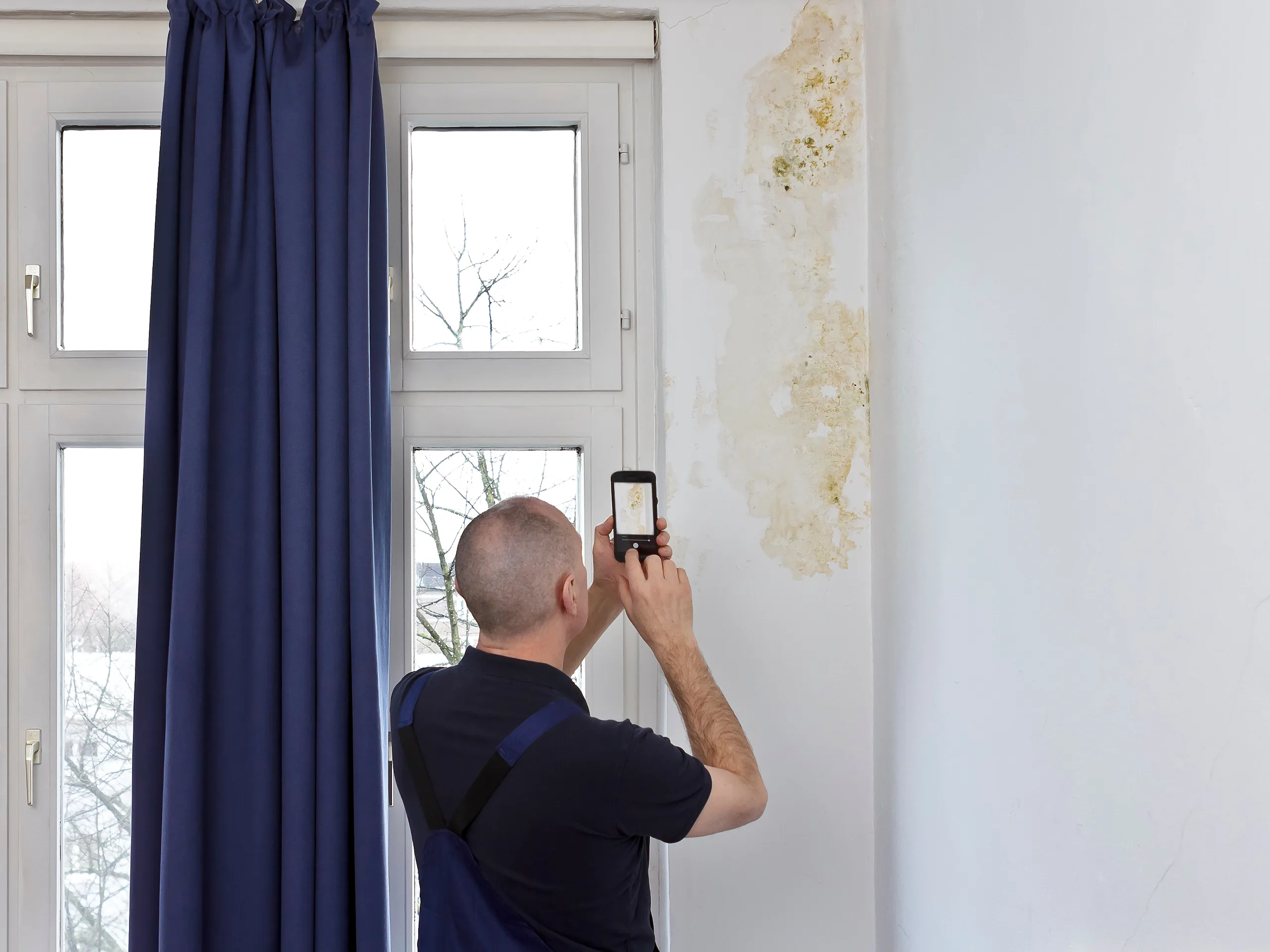 Man taking photos of a wall with a large area of damp