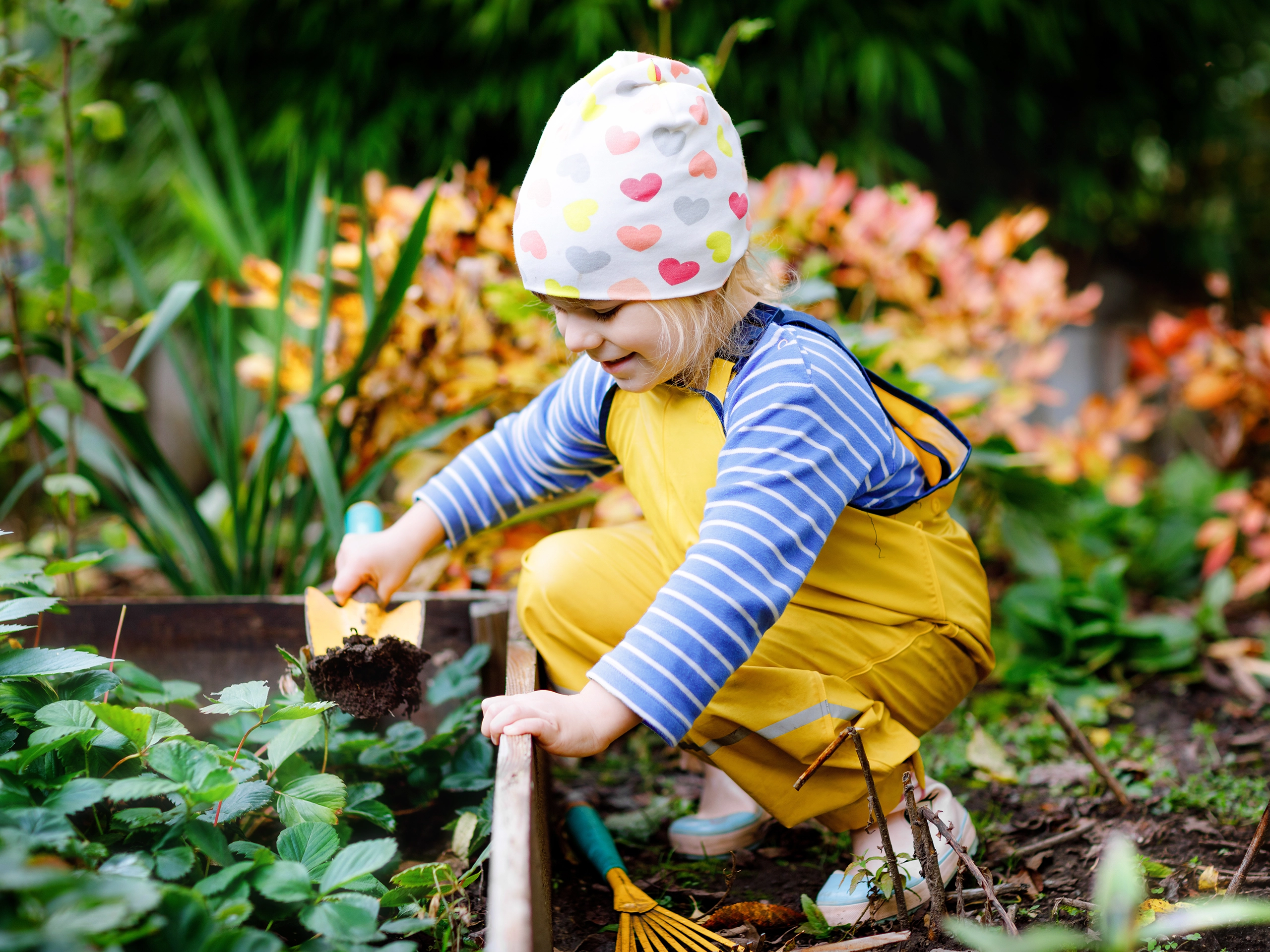 Young girl playing in the garden in flowerbeds