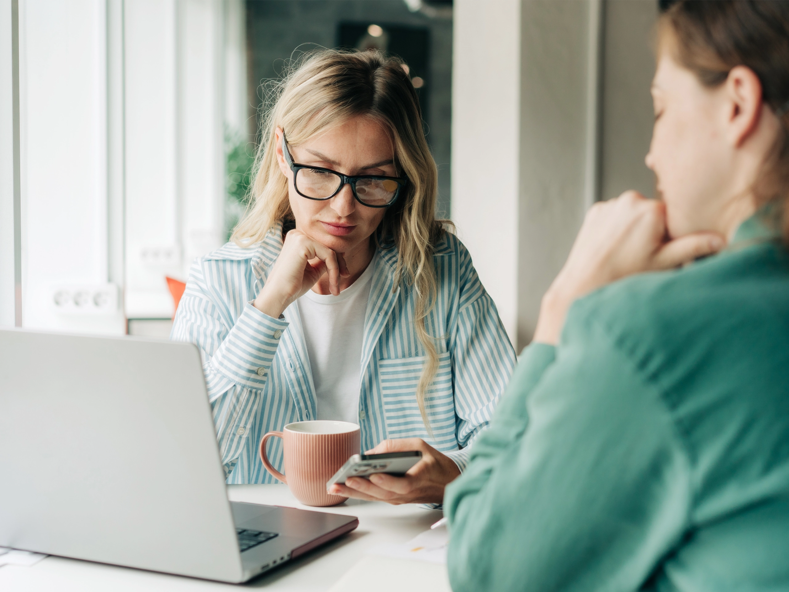 Two female colleagues are discussing a business project in a modern office.