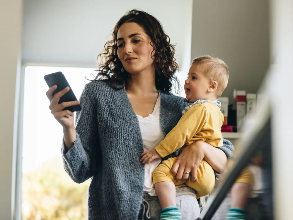 Mum holding her baby while checking on her phone