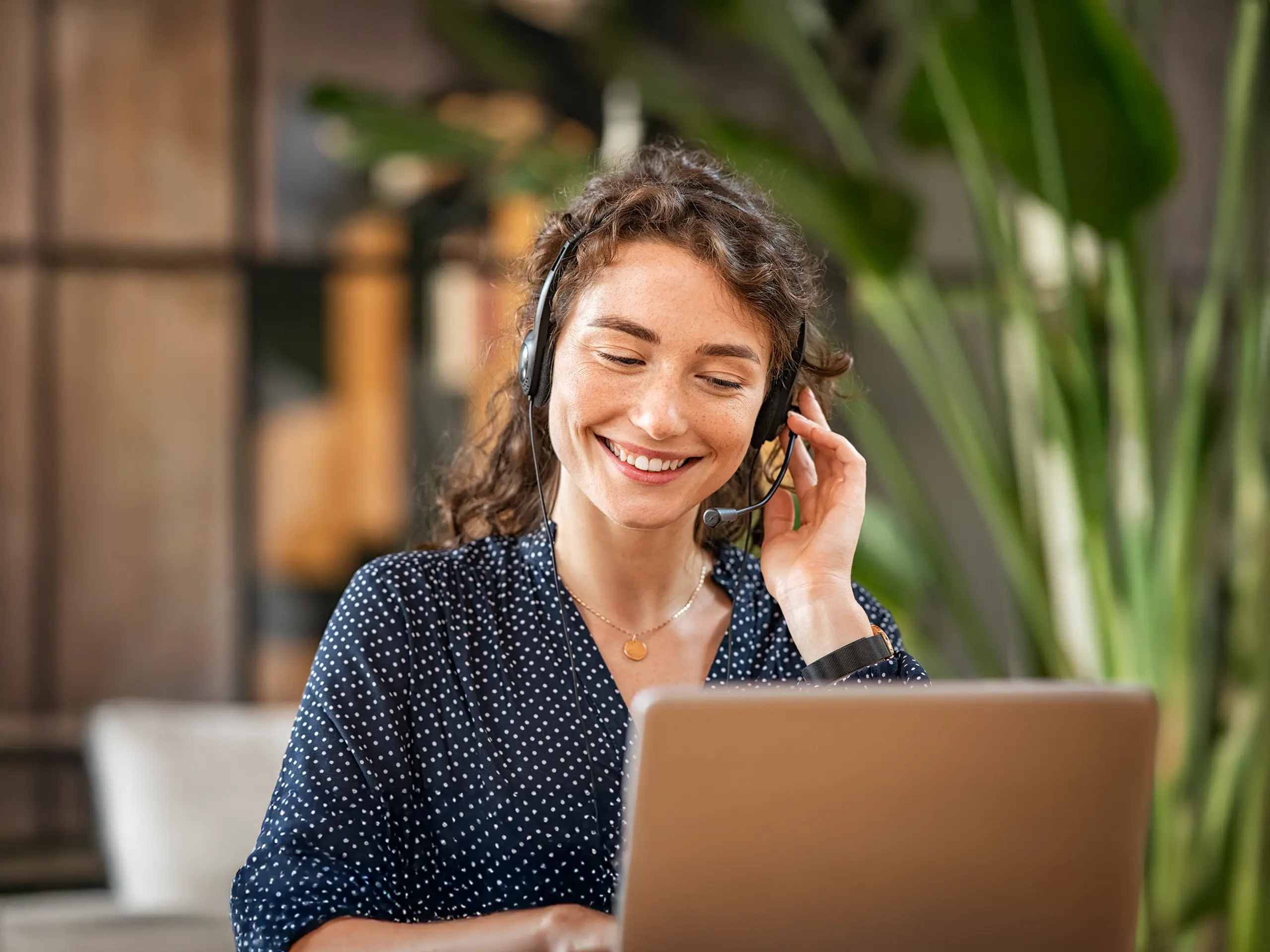 Happy young woman working on laptop while talking to customer on phone. 