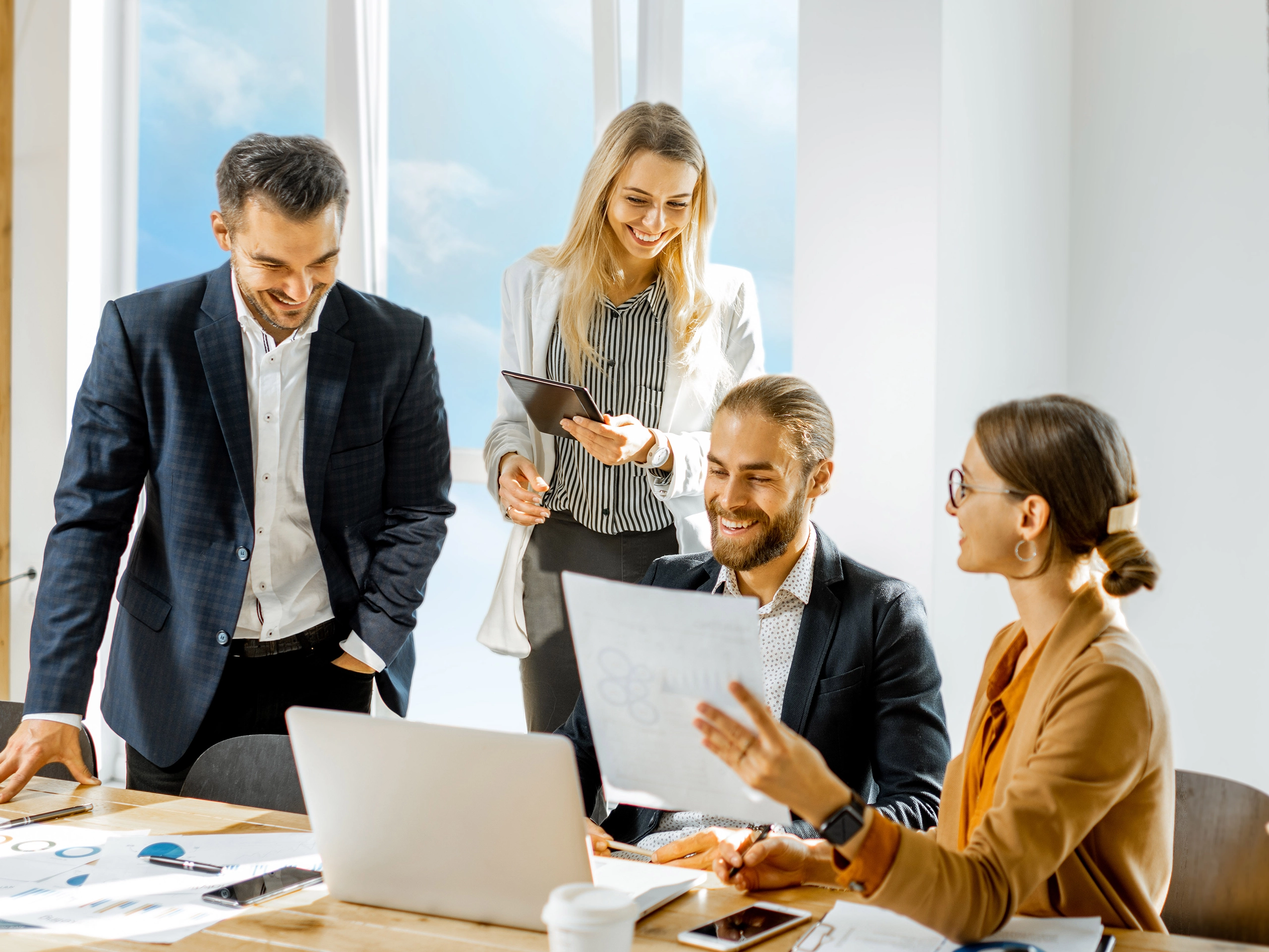 Team reviewing documents together around laptop in bright meeting room