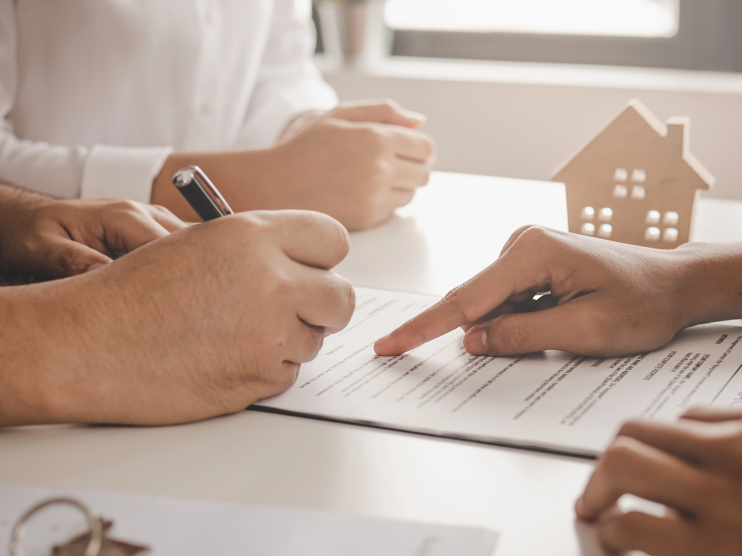Close up hands signing contract document with small house model