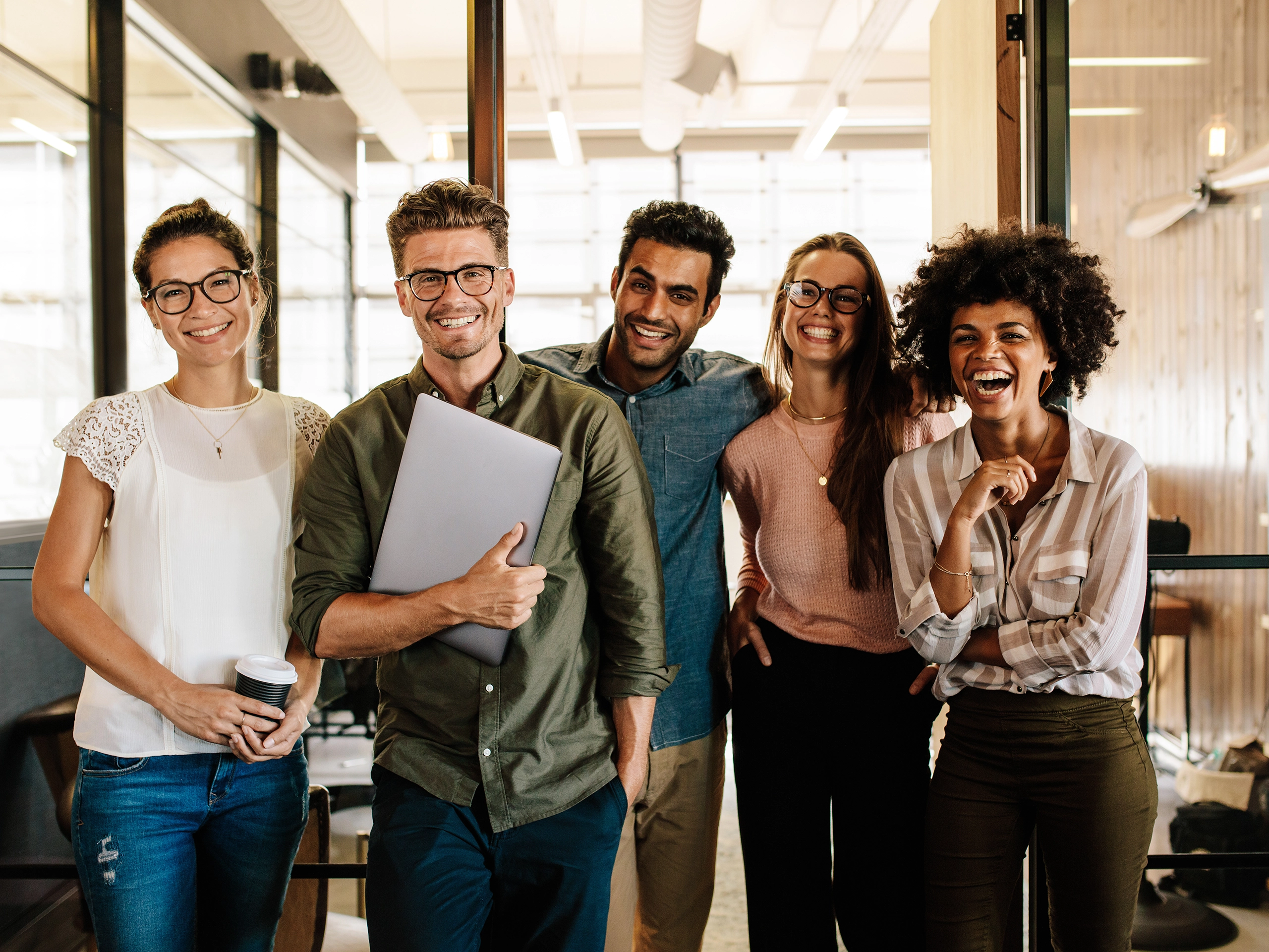 Group standing together holding laptop in modern office corridor setting