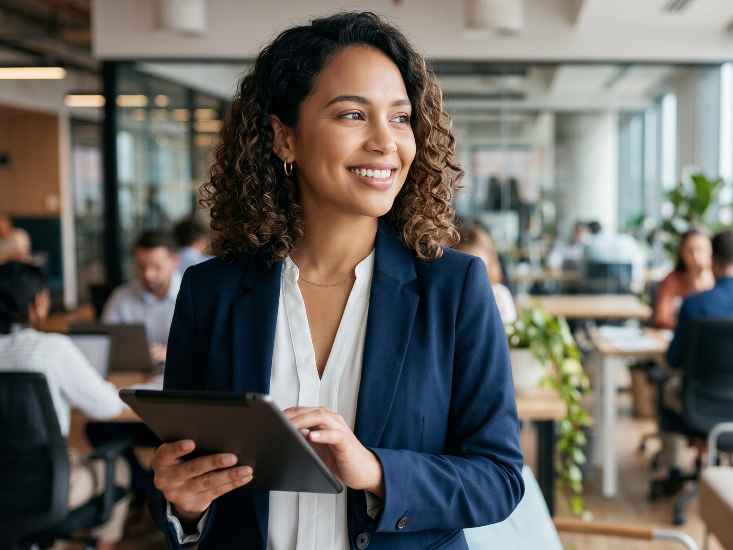 Portrait of happy curly hair businesswoman holding tablet in busy open plan office. Modern female executive, diverse leadership and successful management