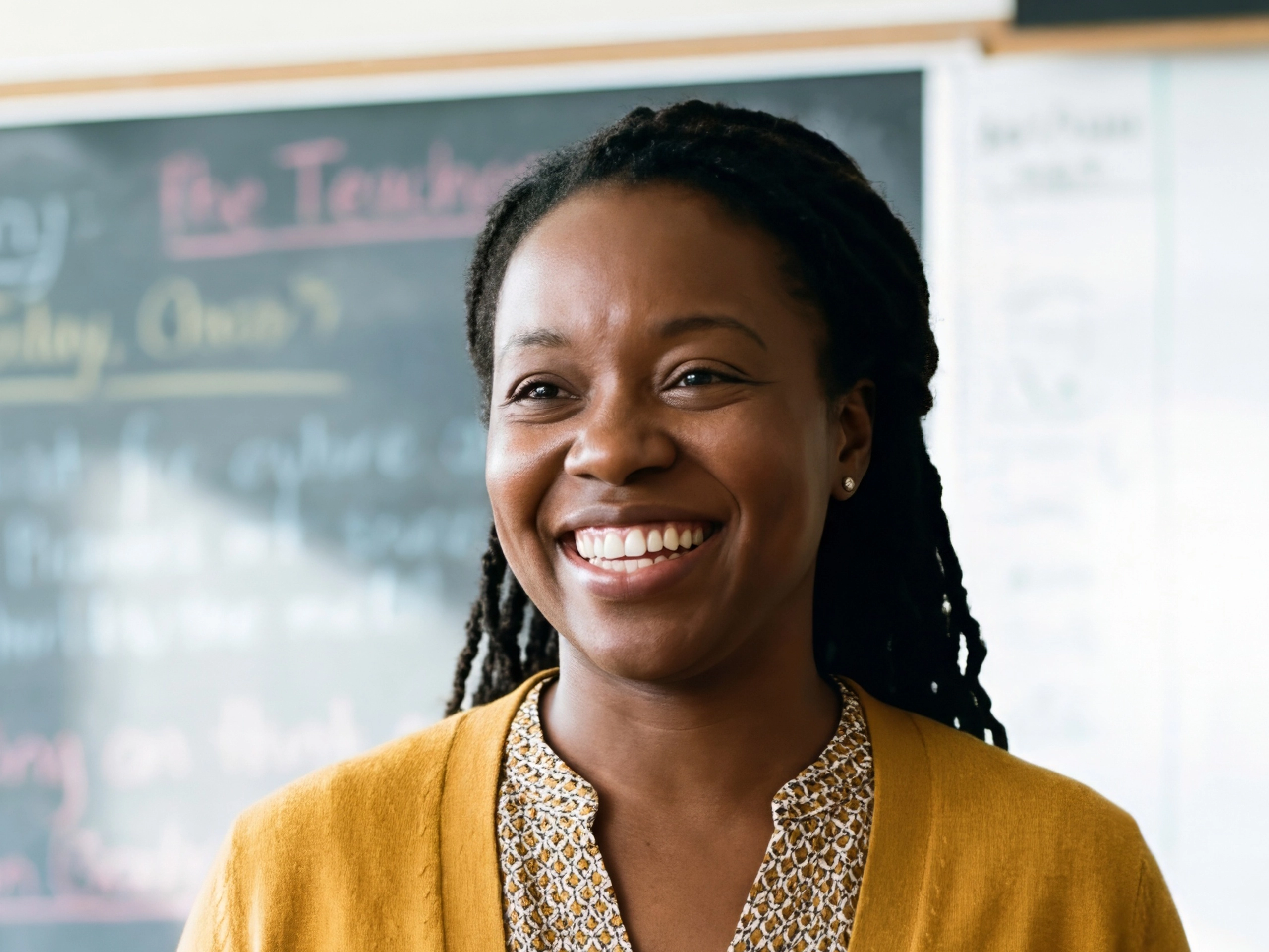 Black woman teacher with dreadlocks standing in classroom with open arms and smiling. Education and welcoming learning environment