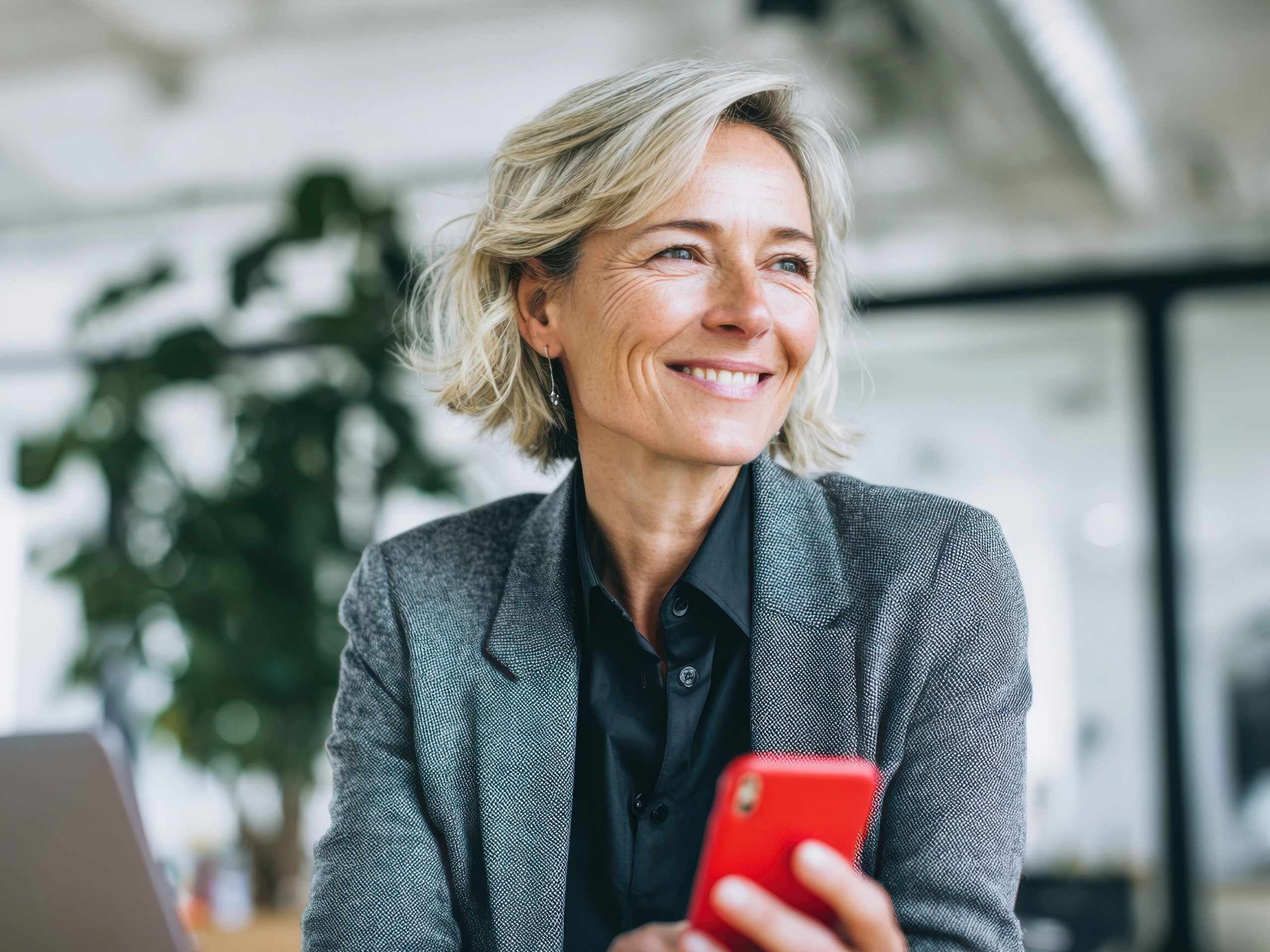 Smiling woman holds phone at work. Modern professional, happy and successful.