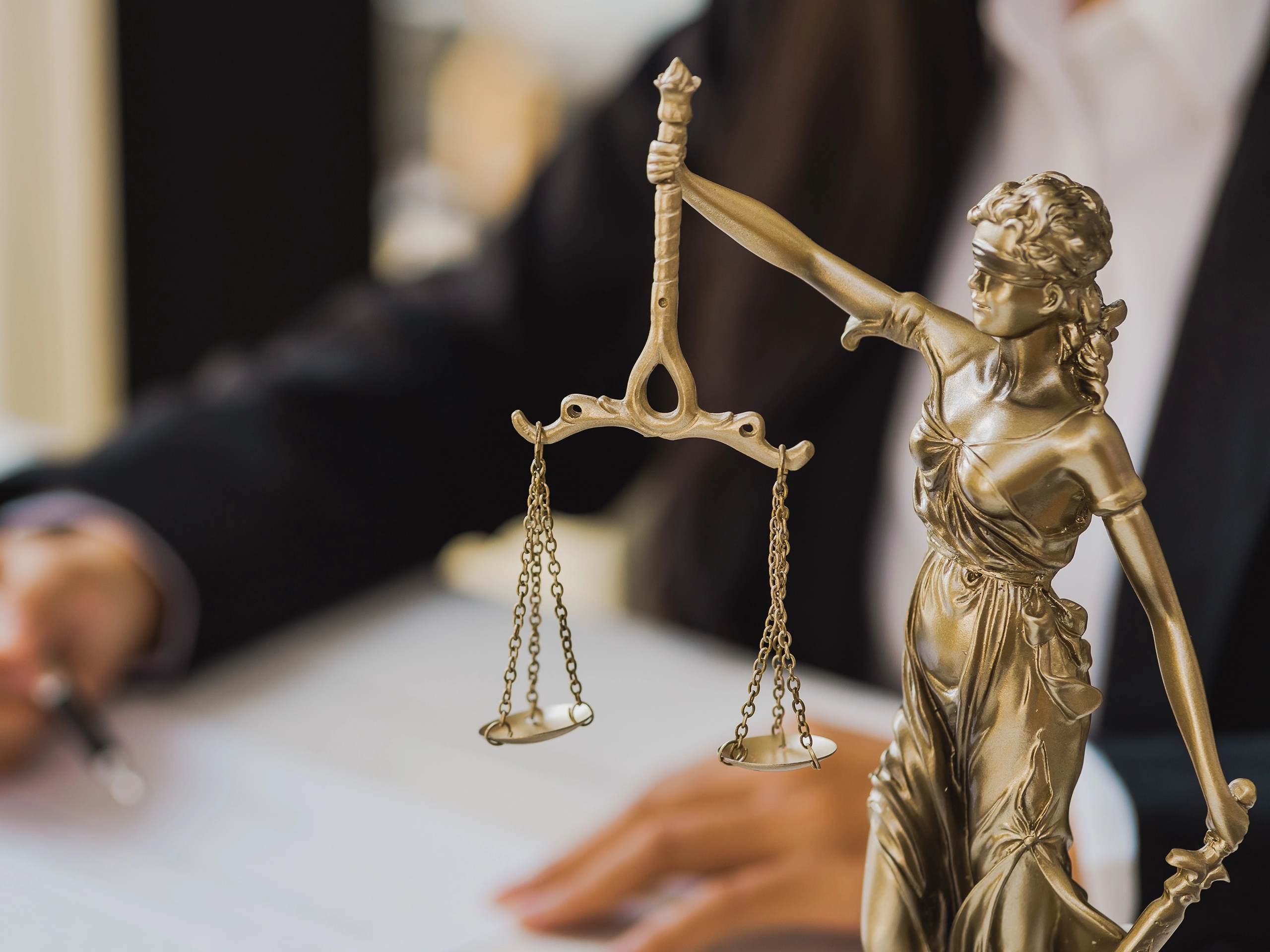 Female lawyer reviewing contract documents with Lady Justice statue symbolising fairness, law, and justice