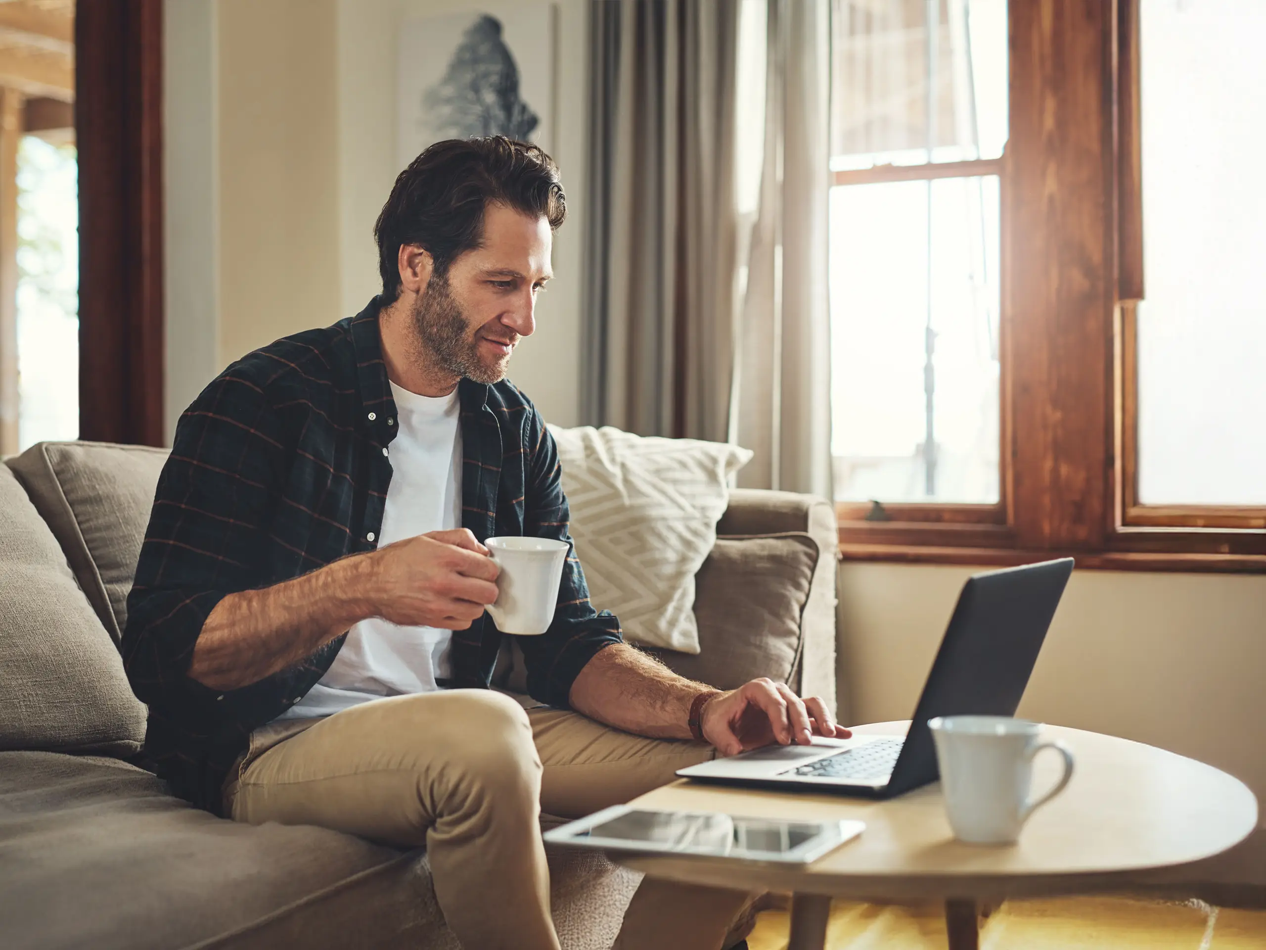 Remote work, laptop and man on sofa with drink, at home.