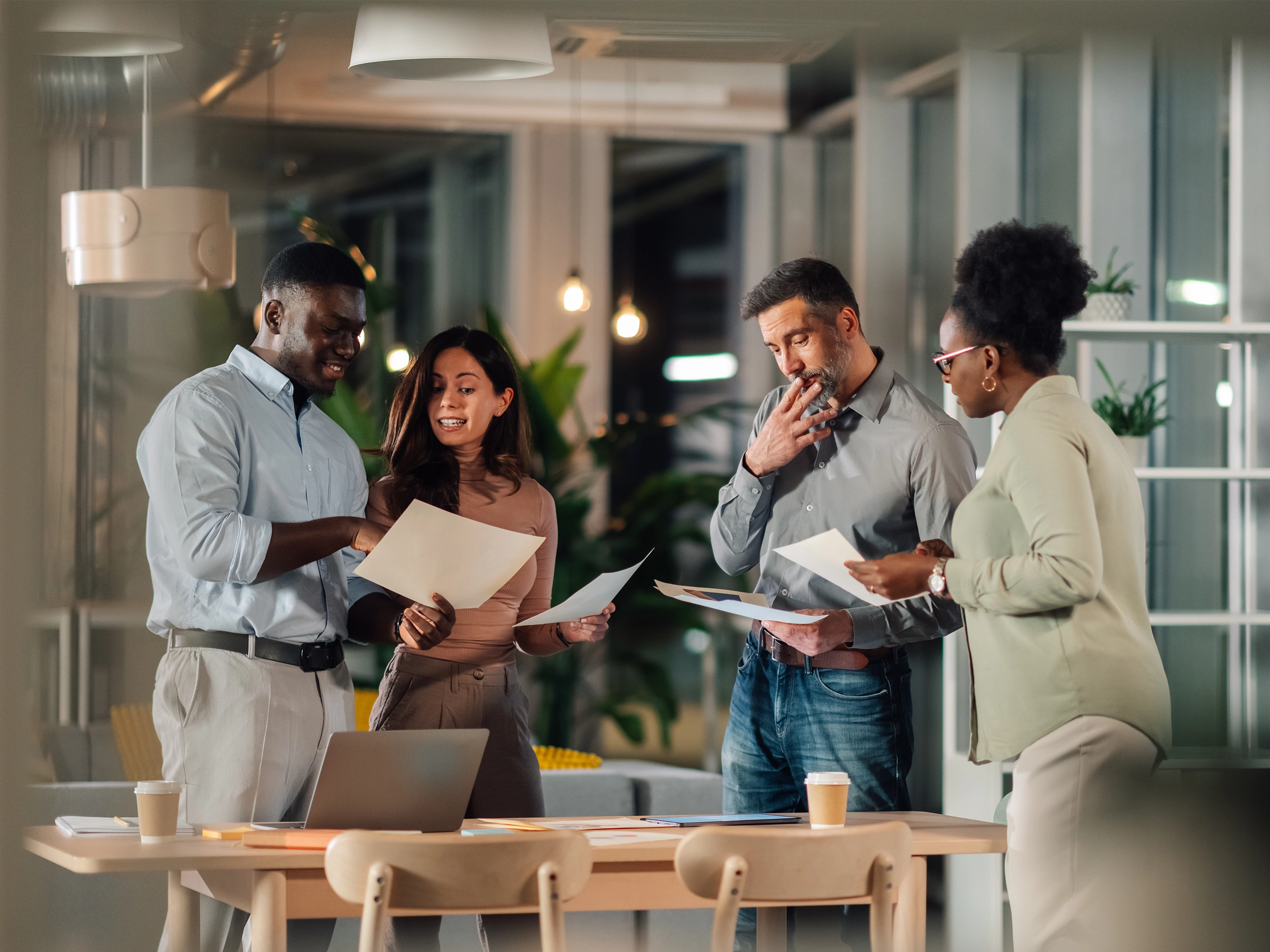 Diverse business people discussing documents and analyzing data in an modern office during an evening work session