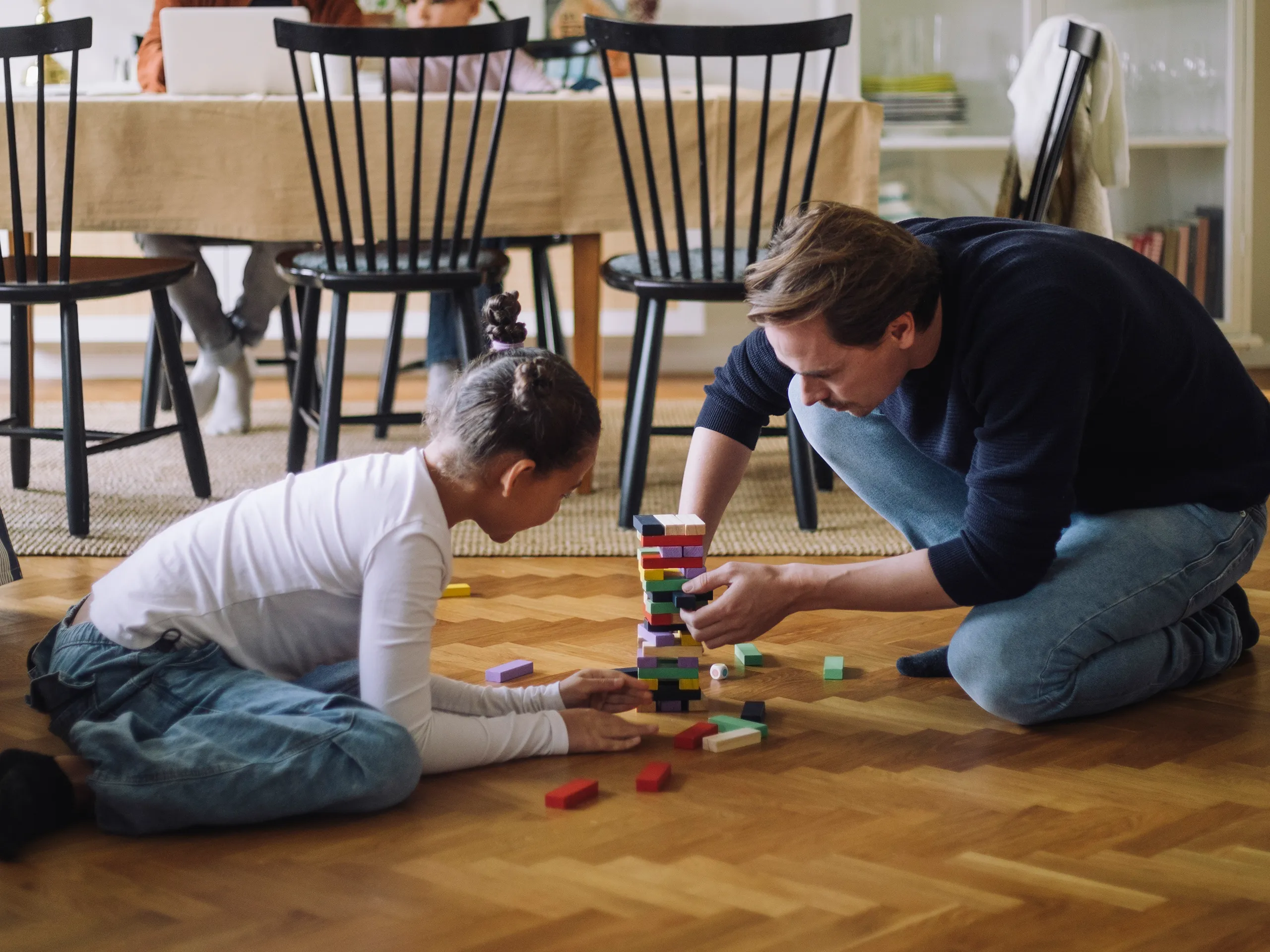 Father and daughter build a tower out of colorful wooden blocks together in the living room.