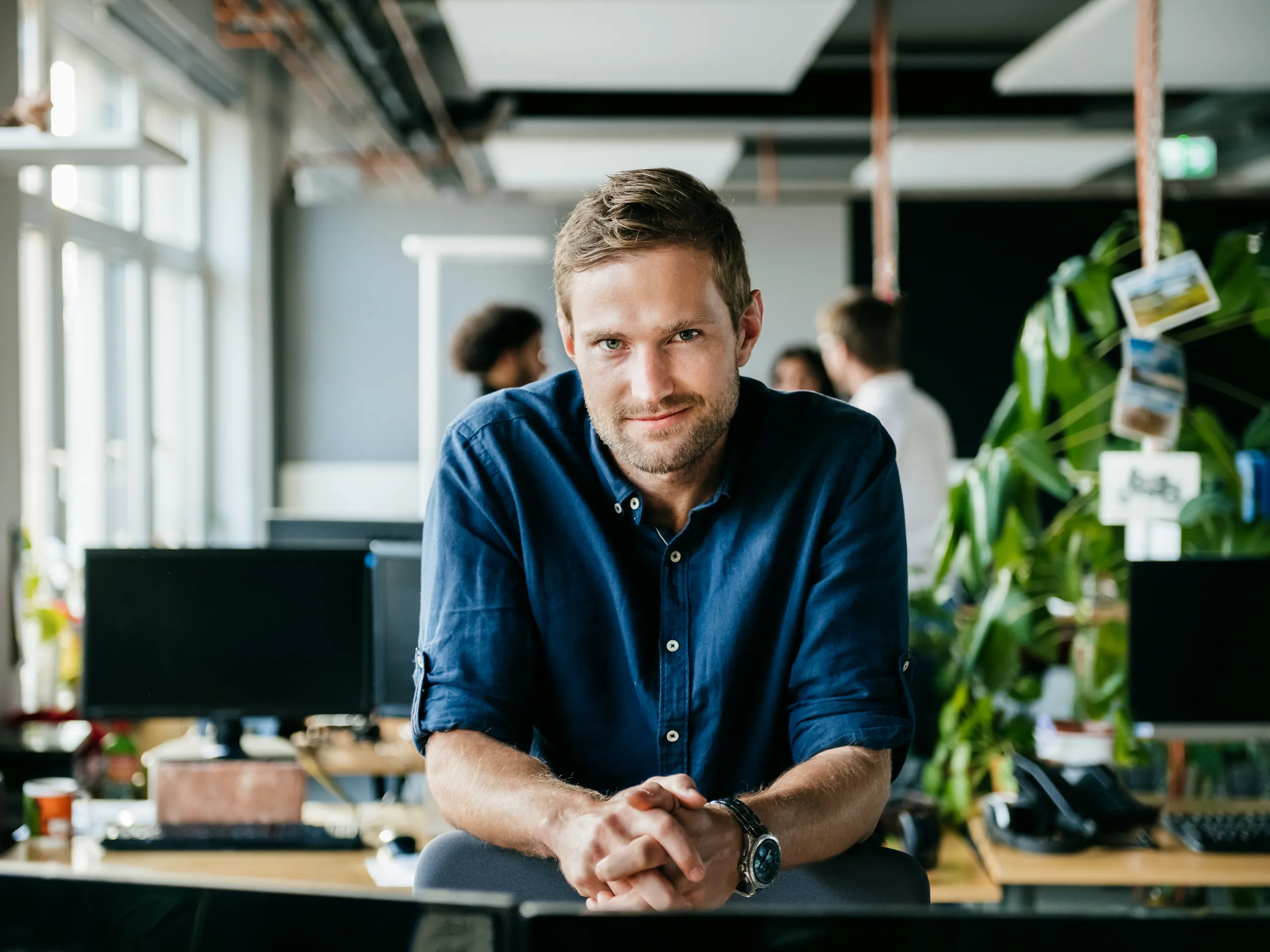 Man in a blue shirt sits at a desk in an office.