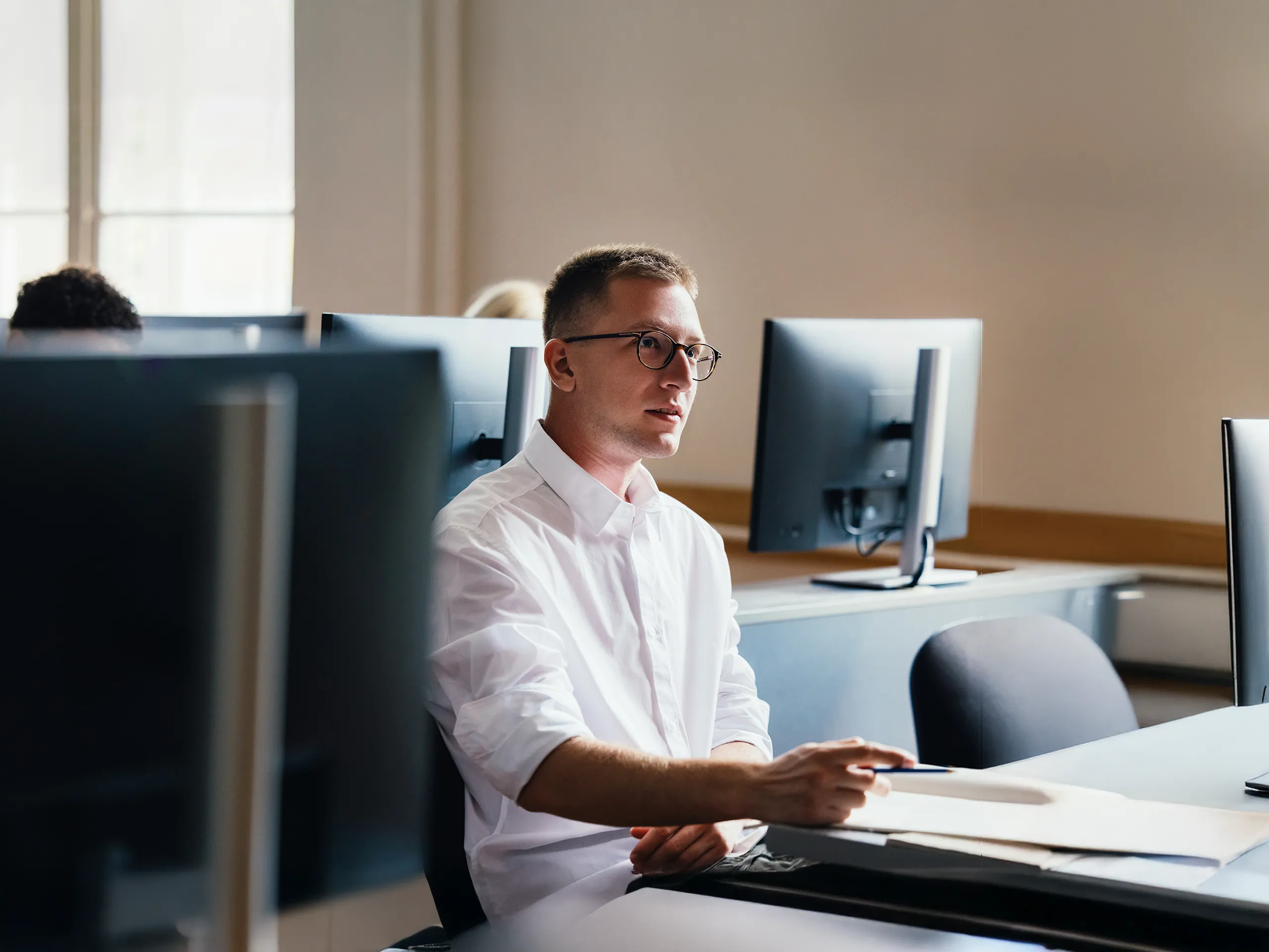 Man works with focus using a laptop and documents at a wooden table.