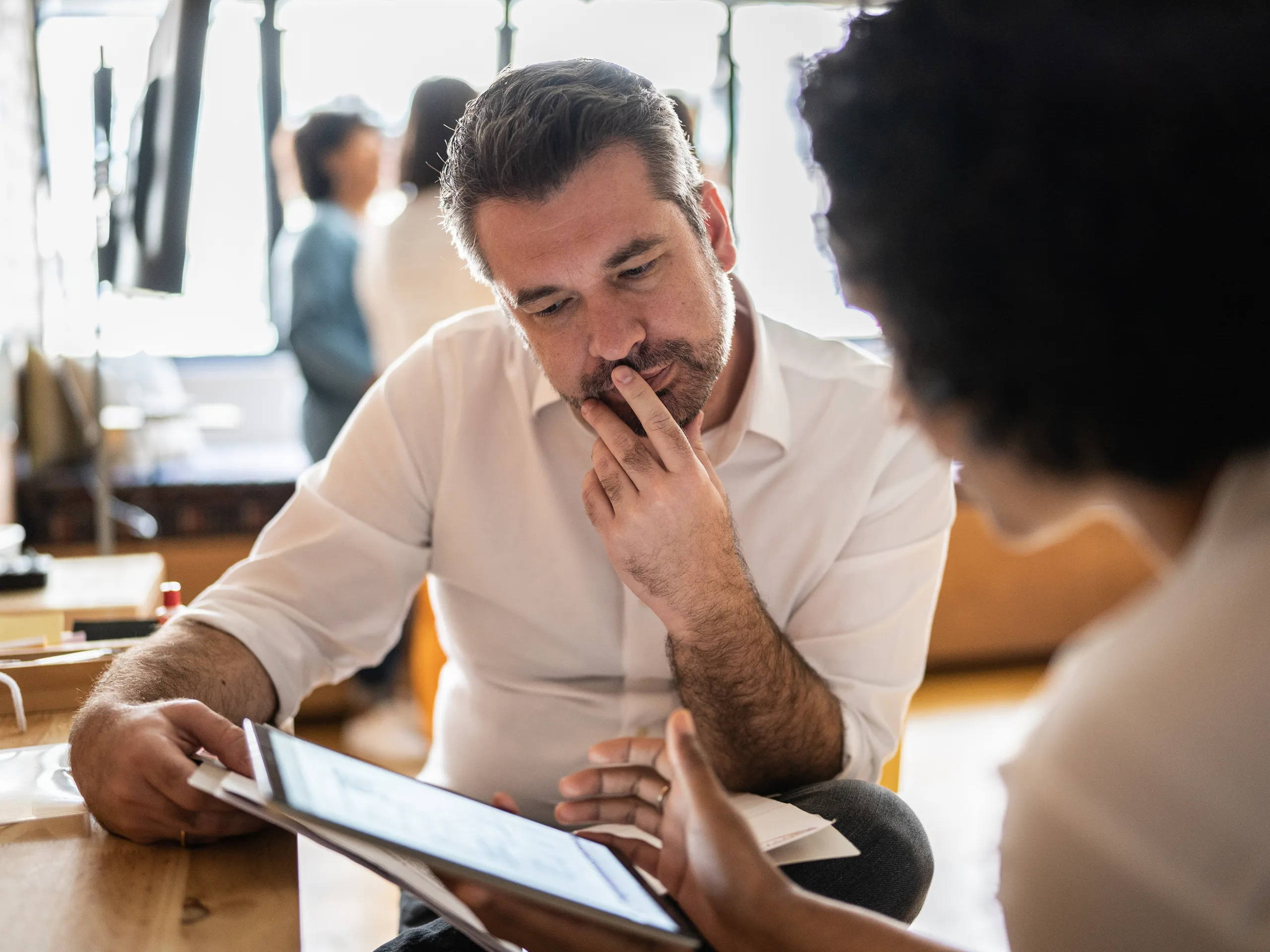 Man in a white shirt looks thoughtfully at a tablet.