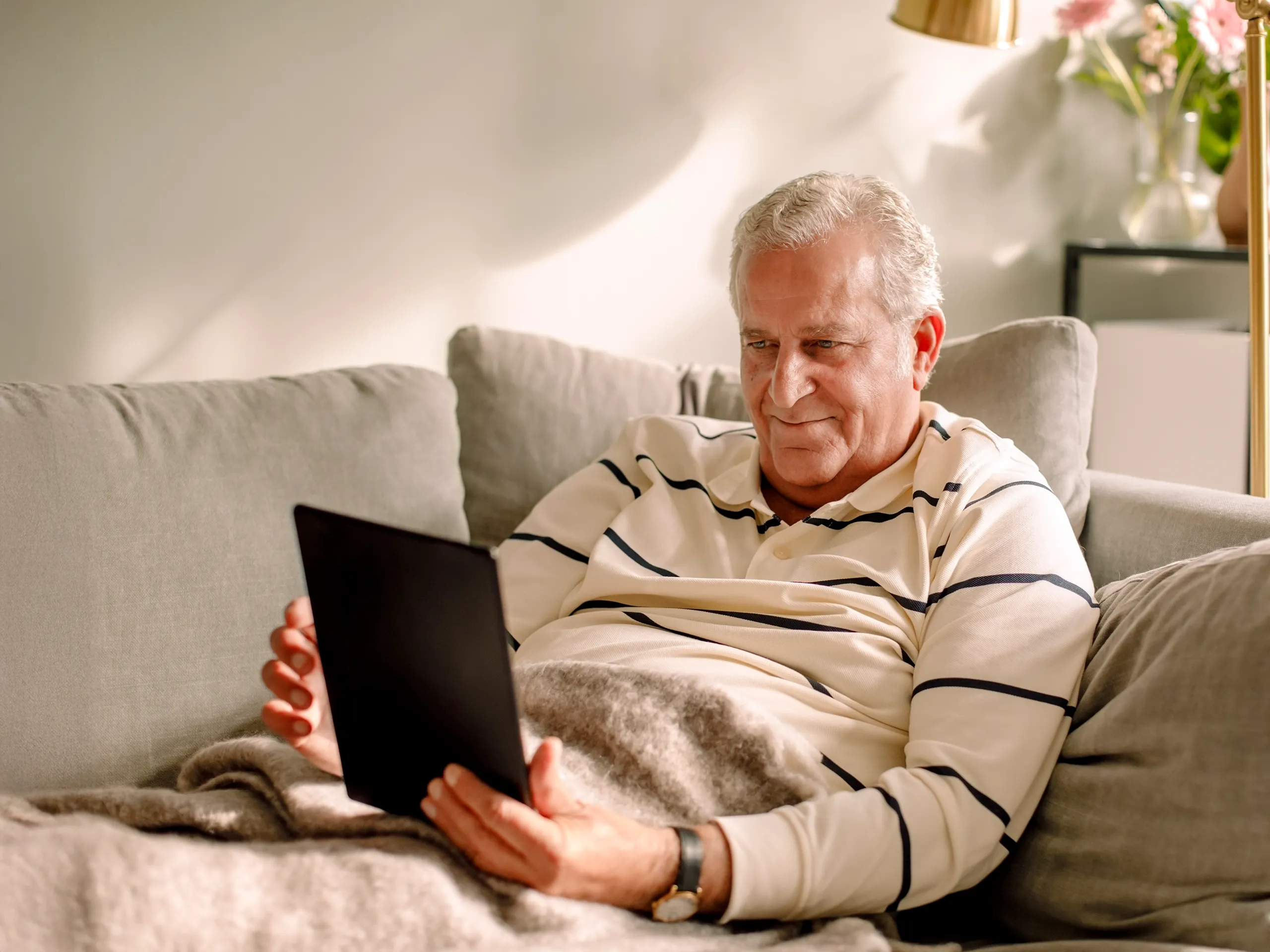 Older man relaxing on a sofa, looking at a tablet.