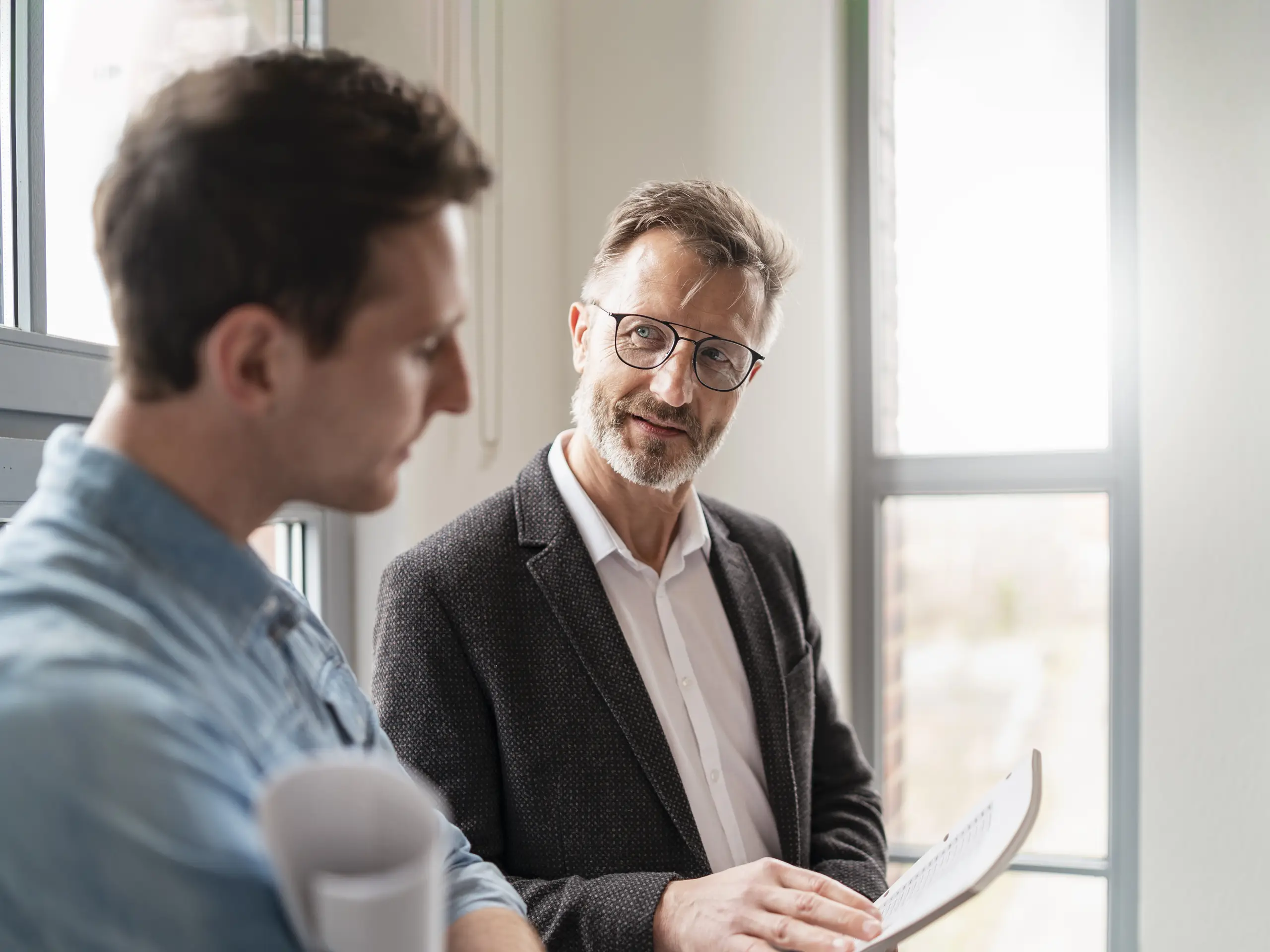 Two people in an office discussing documents in a bright workplace setting