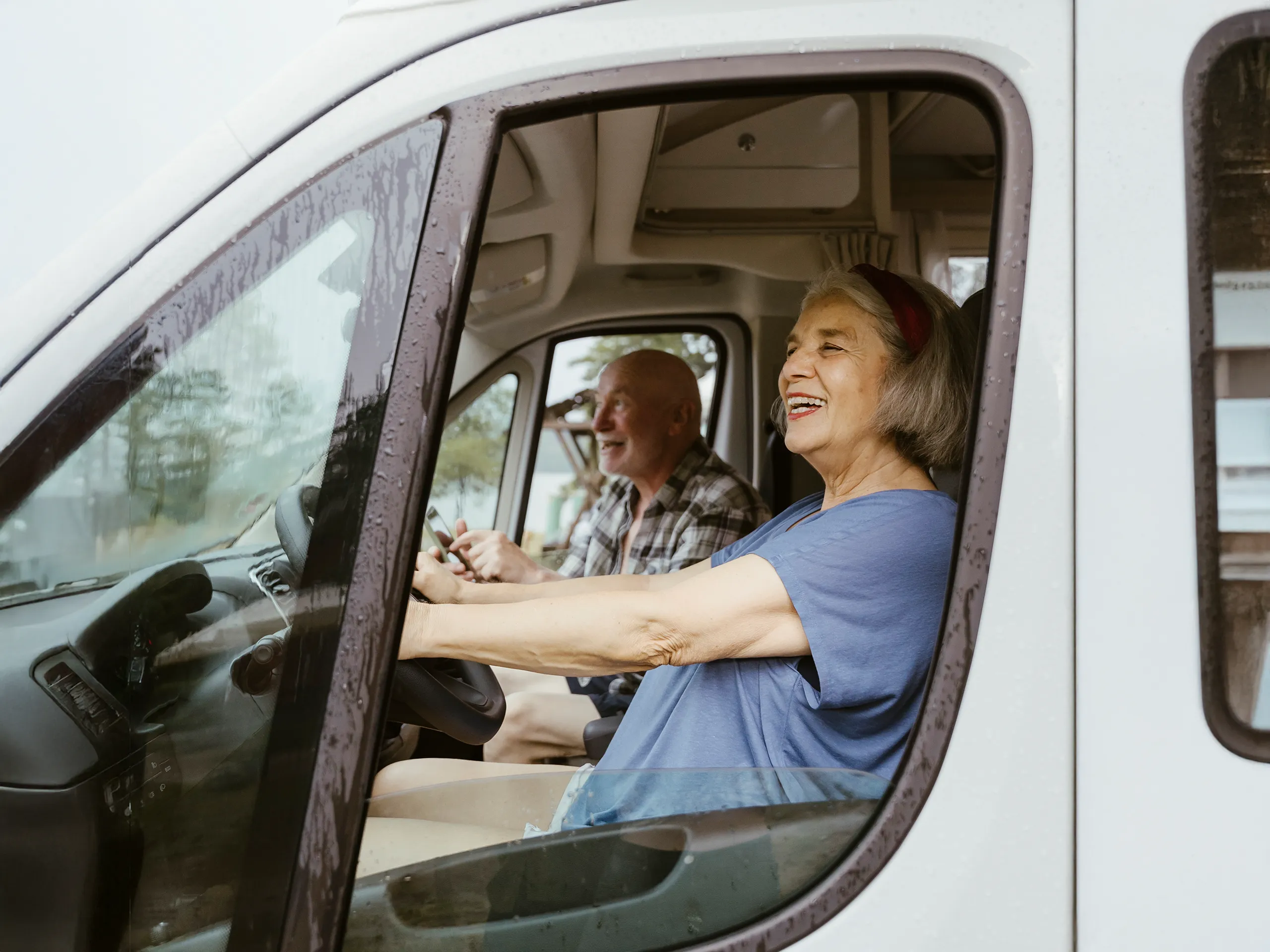 Older couple laughing while driving a motorhome in the rain.
