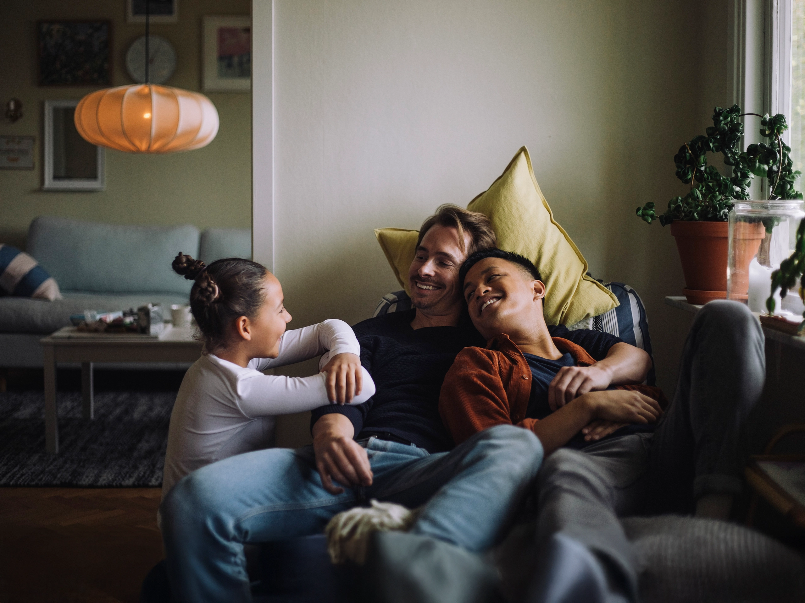 Two dads cuddling with their daughter on the couch while laughing.