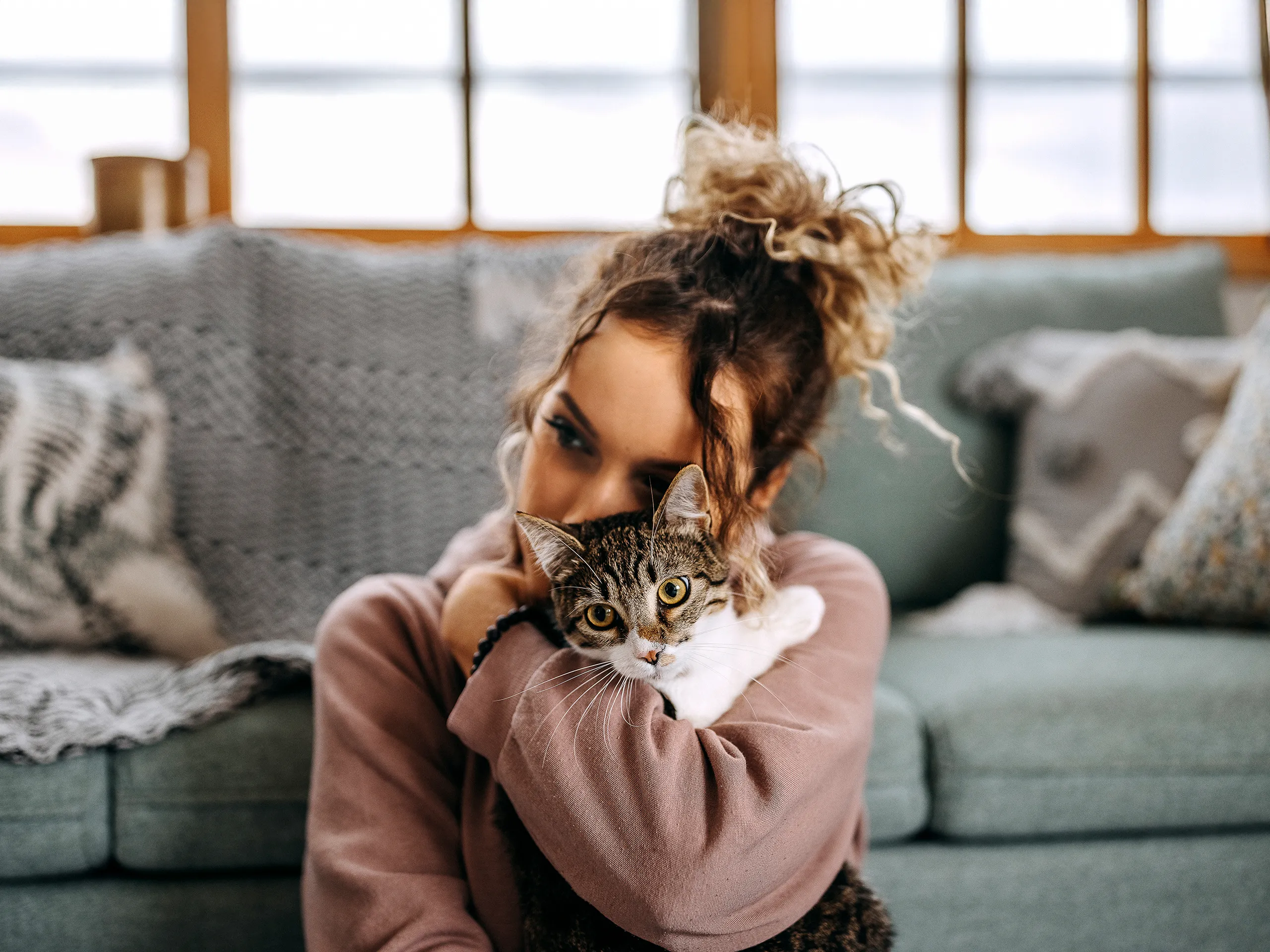 Young woman cuddling a tabby cat in a cozy living room.