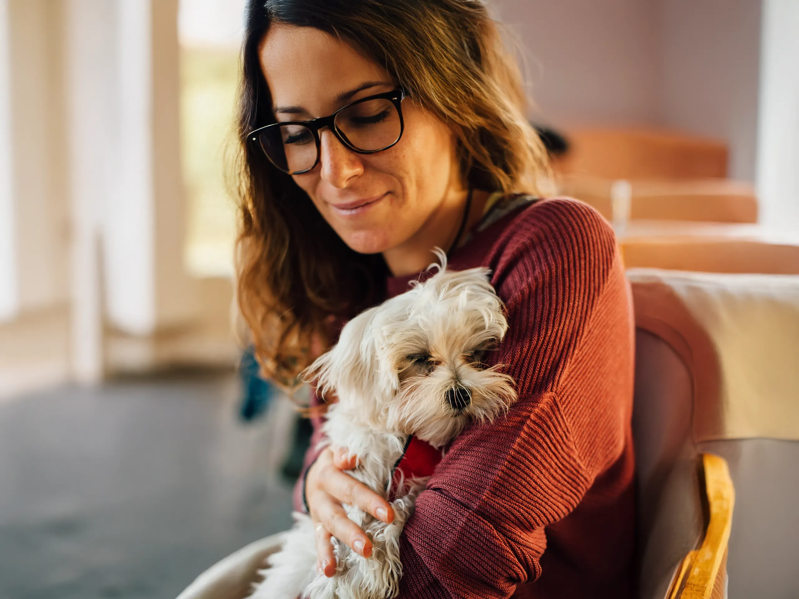 Woman with glasses and brown hair holds a small white dog in her arms.