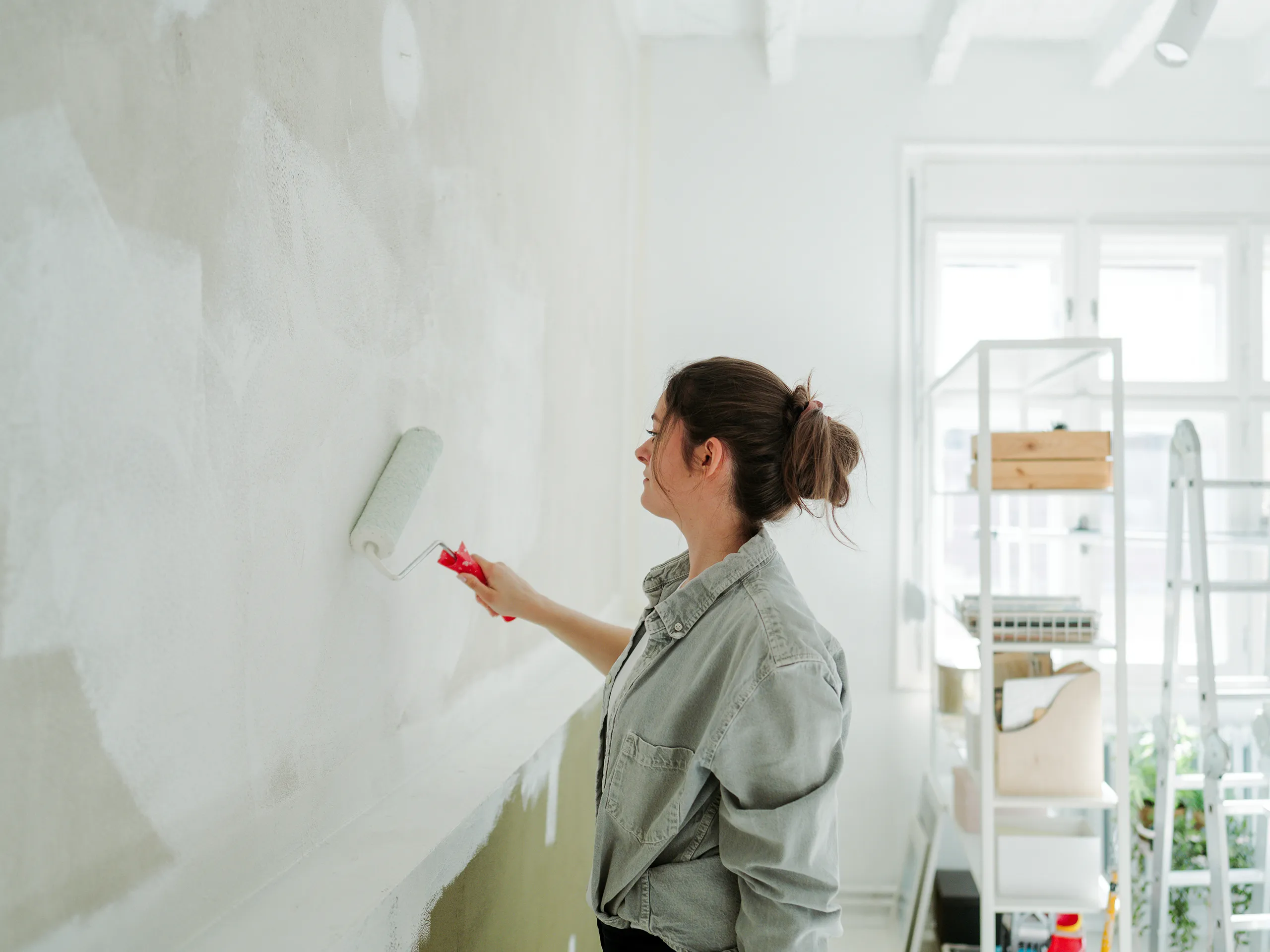 Woman paints a wall with a paint roller in a bright room.