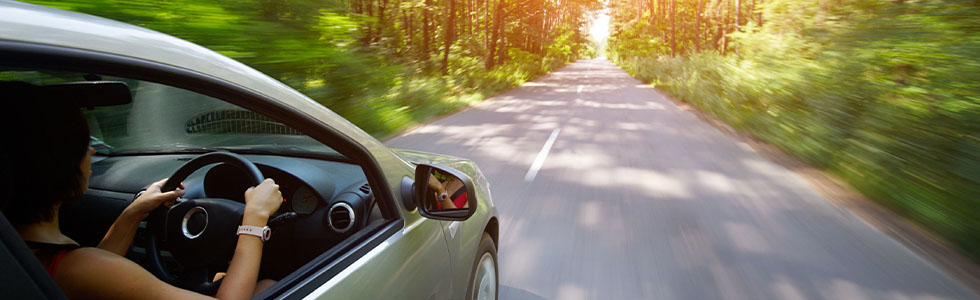 A woman driving a car through a wooded road
