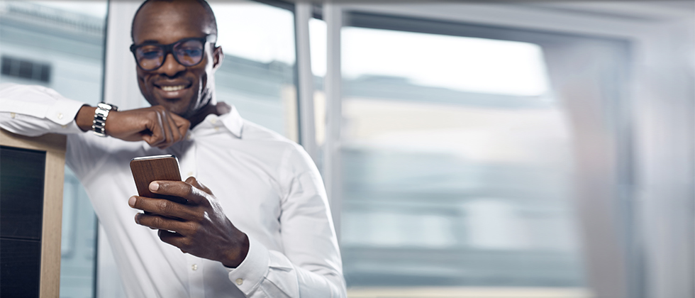 Coloured businessman smiling and looking down at mobile phone